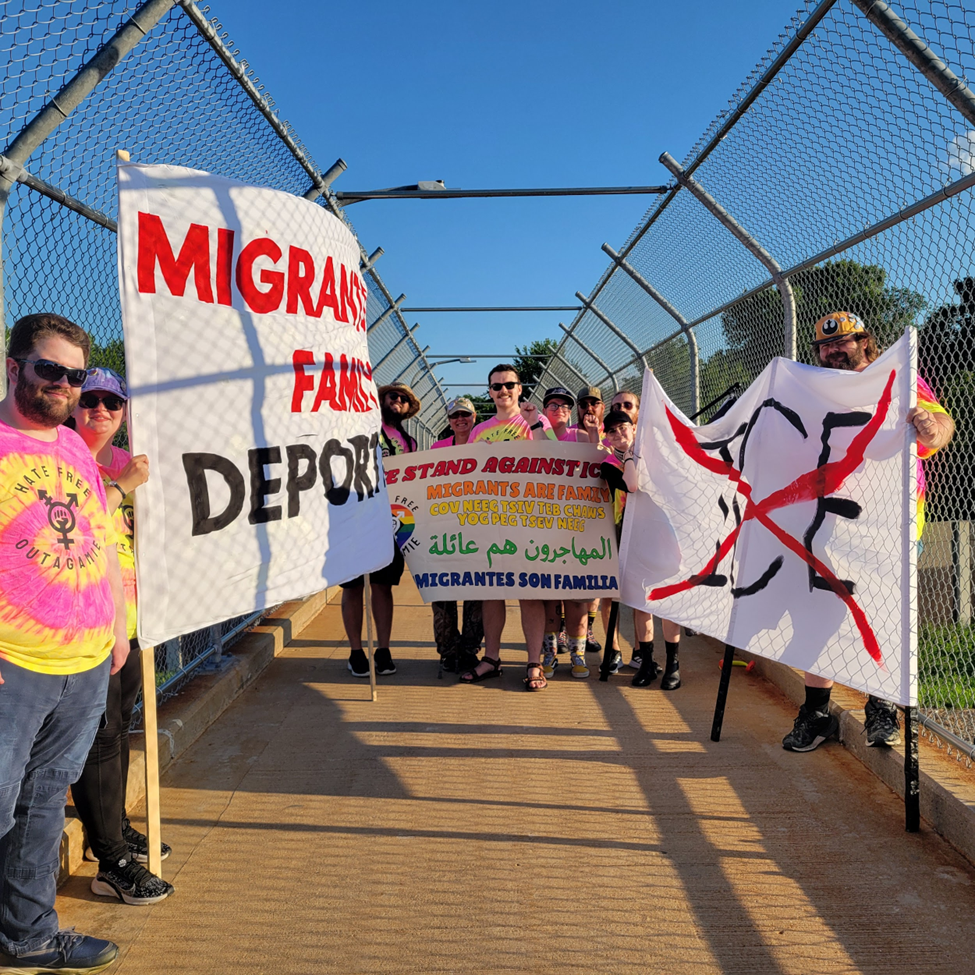 A group of protesters holding banners on a pedestrian walkway above a highway.
