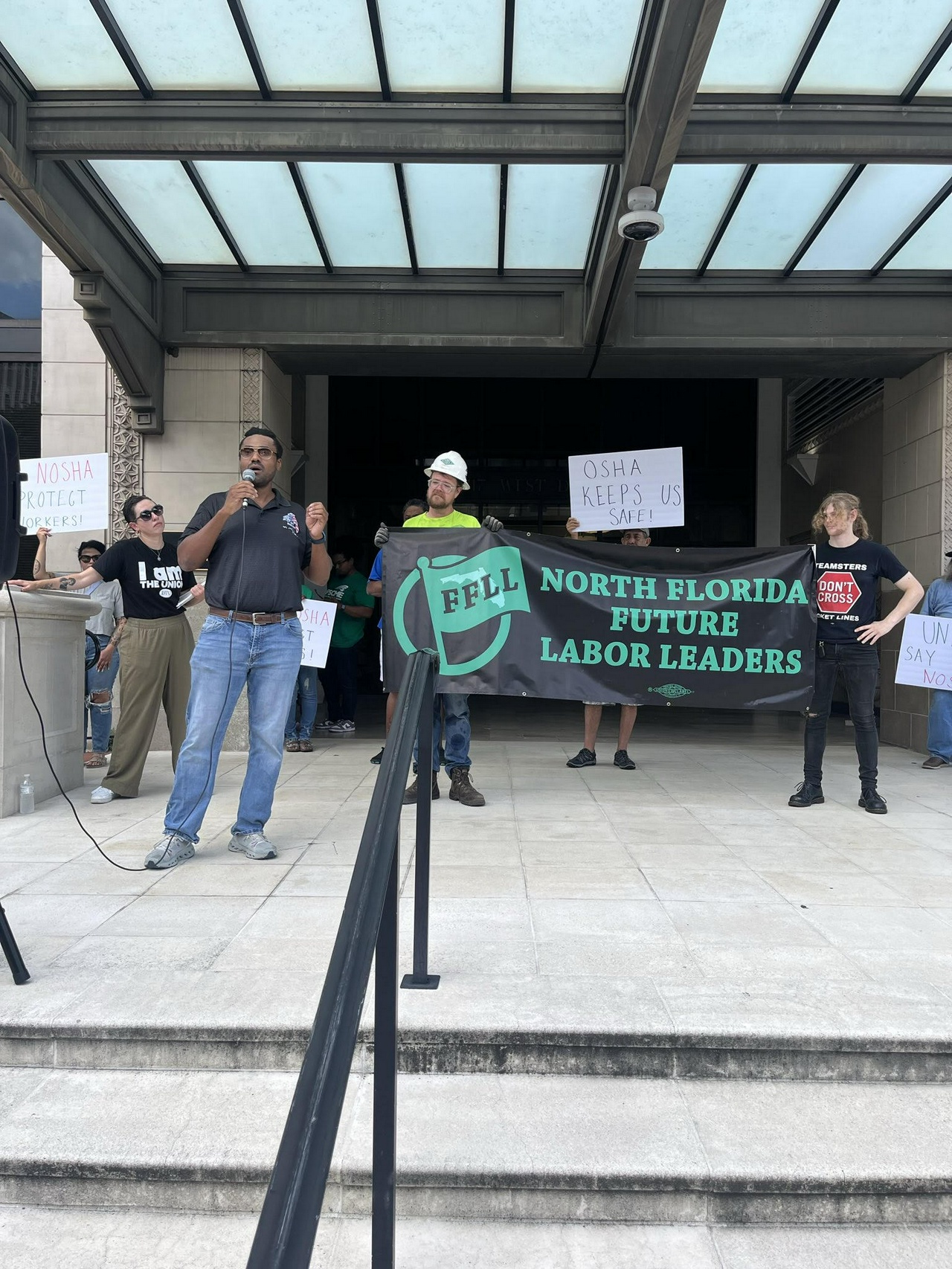 A protester speaks in front of a banner.