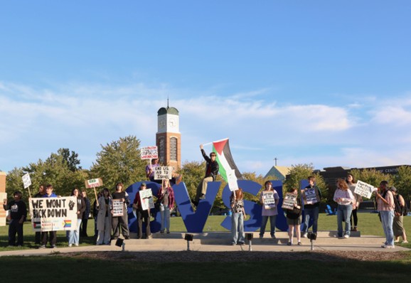 Caption can read: Students rally in front of the GVSU sign on Allendale campus.