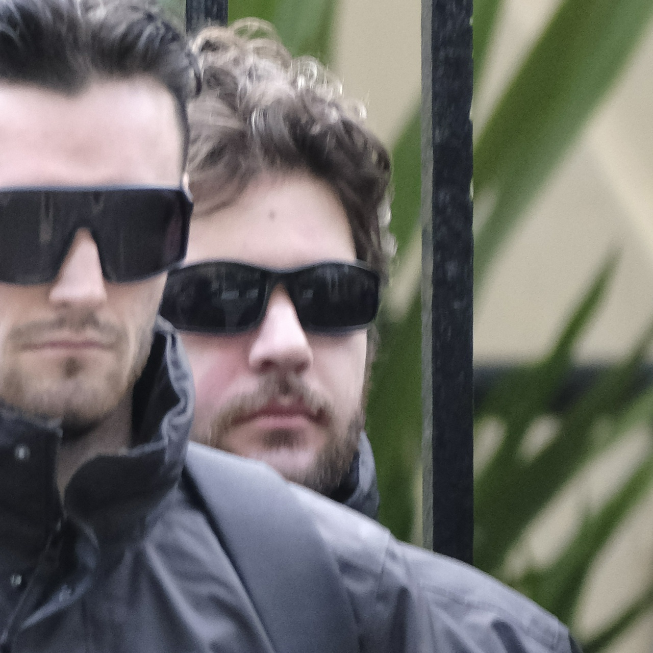 A shorter man with brown curly hair, flushed cheeks and a beard peers over someone's shoulder