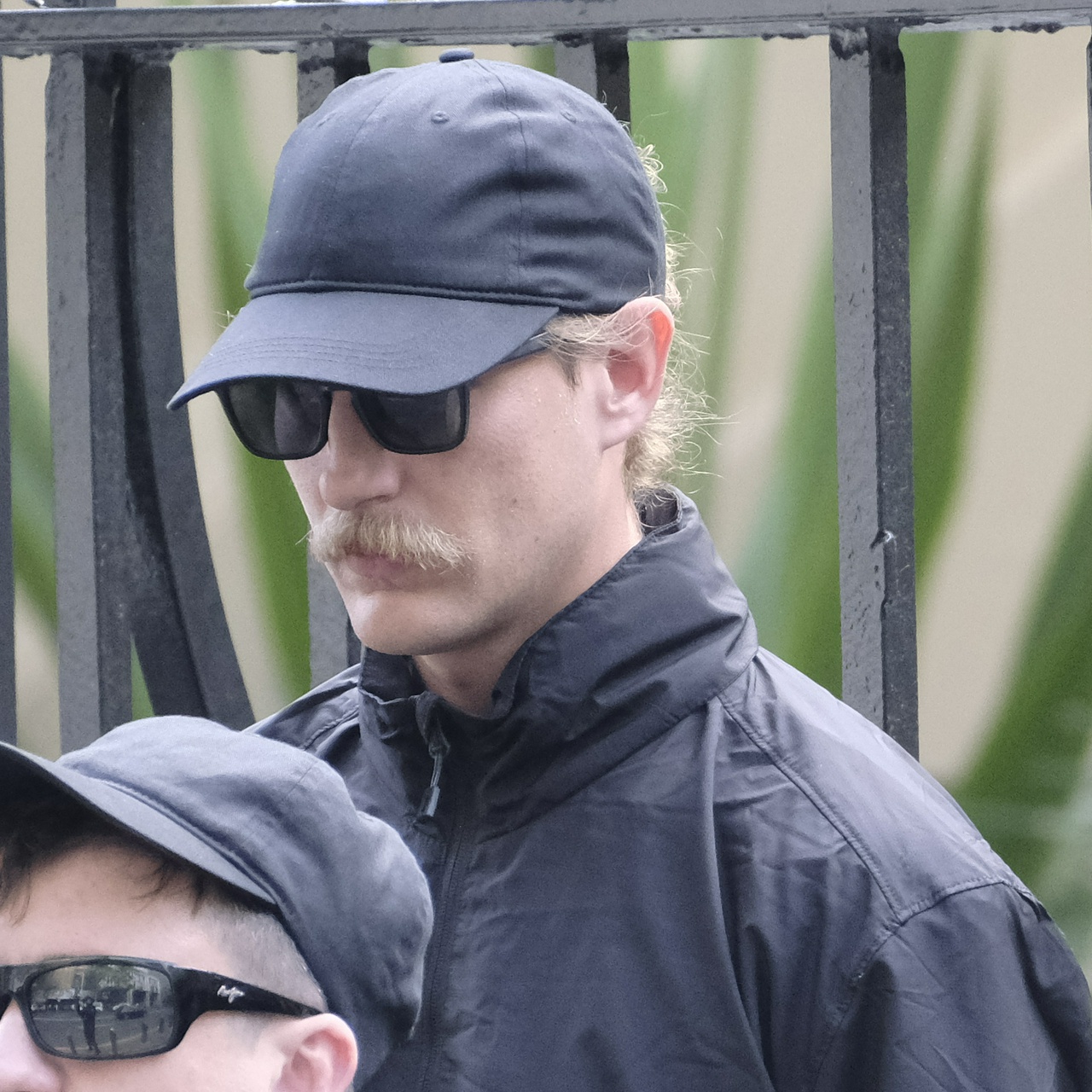 The same man from another angle, ducking his head behind his cap to avoid the camera