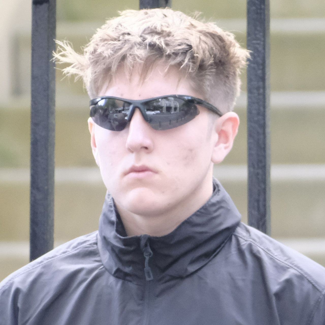 A tall young ginger guy, with pockmarked cheeks, messed up hair and strangely angled sunglasses
