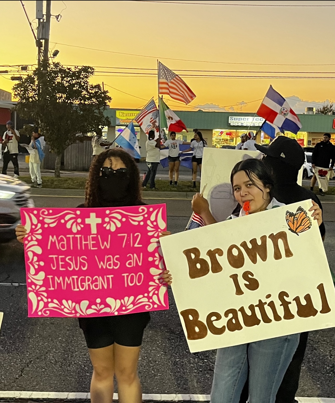 Two protesters hold up signs in support of immigrants while behind them more demonstrators stand on the median of Williams Blvd proudly waving Mexican, Honduran, Dominican and American flags. | Fight Back! News Two protesters hold up signs in support of immigrants while behind them more demonstrators stand on the median of Williams Blvd proudly waving Mexican, Honduran, Dominican and American flags.
