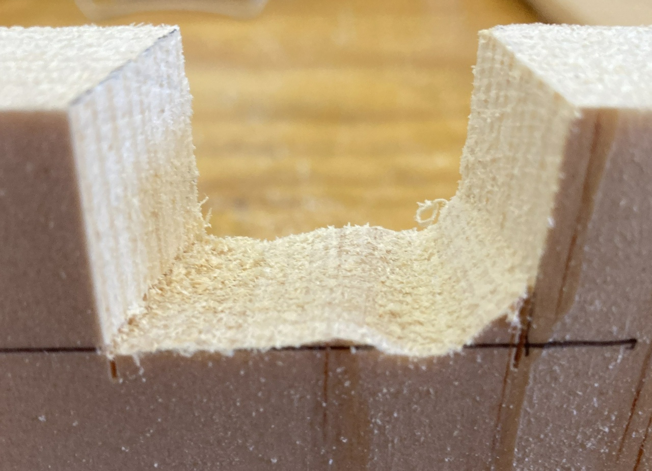 Waste partially cut out between dovetail pins. The bottom of the space is wavy with a chunk of extra waste yet on the right