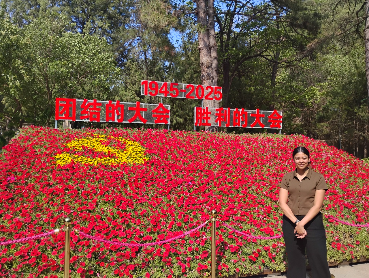 A woman standing in a bed of flowers which were planted to resemble the flag of the Communist Party of China.