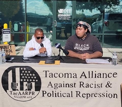 Participants in Tacoma press conference demand justice for Ronald Harris. | Fight Back! News Two people sitting at a table speaking into a microphone.