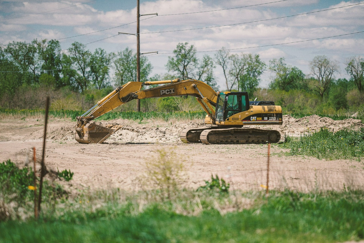 a yellow back hoe sits in a dug up field surrounded by trees and grass photo by Brian Statler via UnSplash