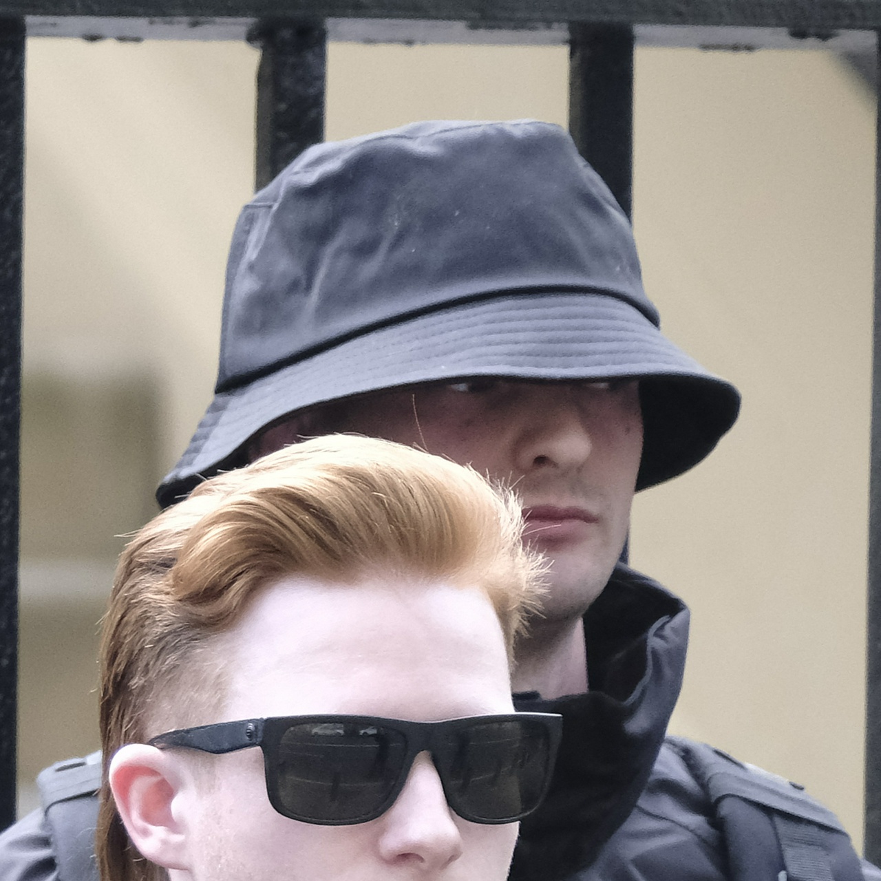 A weary looking man with a short face hides in a bucket hat, glancing sideways nervously. He has two X's tattooed behind his right ear