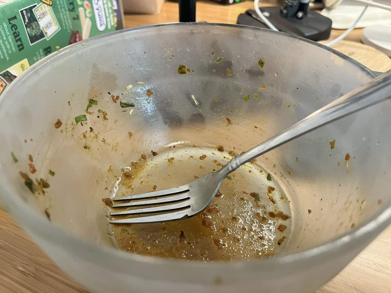 an empty glass bowl containing a fork and some remains of chicken sludge and scallions