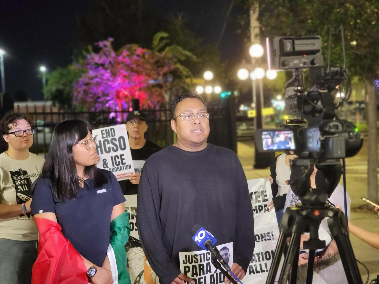 People speaking at a press conference holding signs.