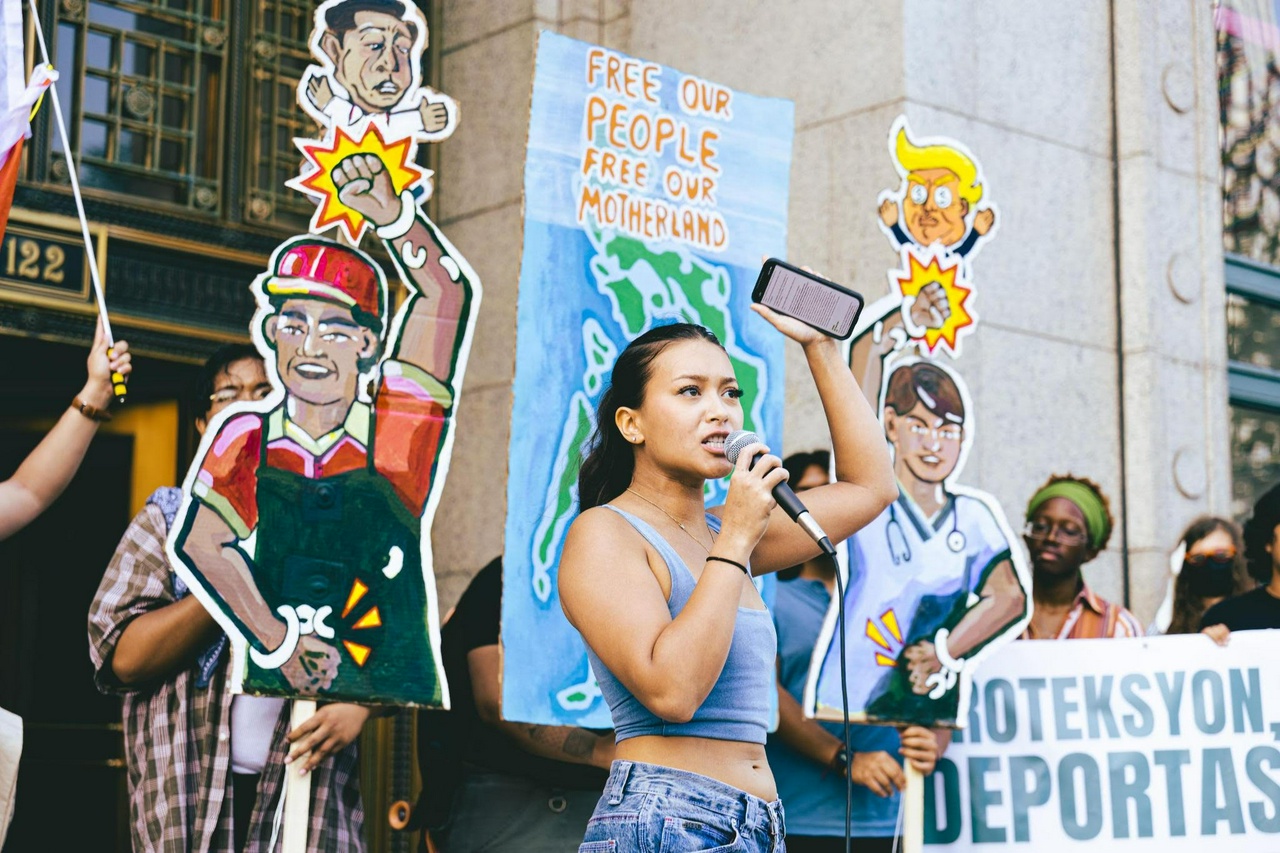 A protester speaks into a microphone in front of cut out graphics signs.