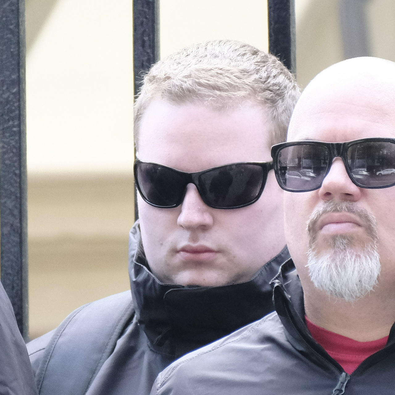 A round blonde guy with a thick neck and bug-eyed wrap-around sunglasses retreats into his own jacket collar