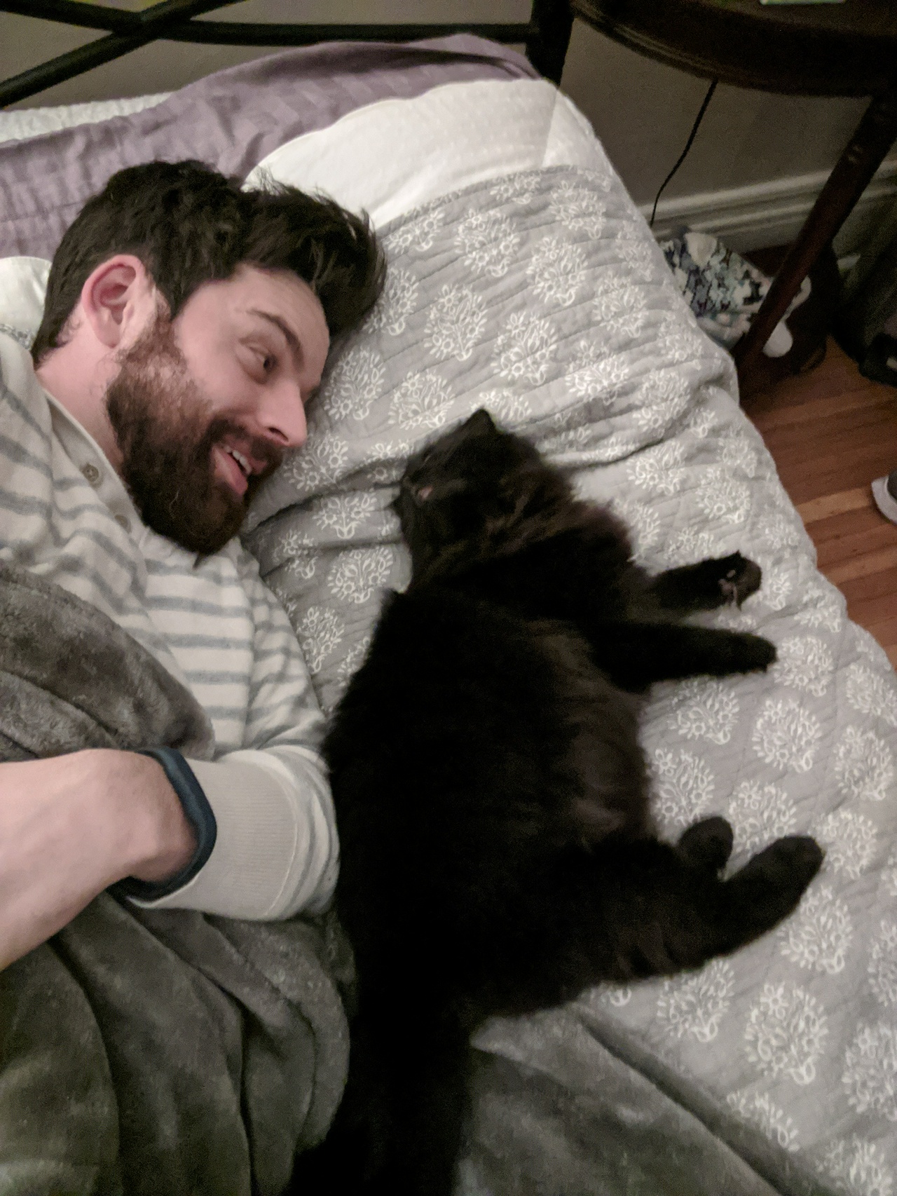 Me and Taggy relaxing on a bed, with Taggy to her right. Her back is towards me, but she turns her head to look me in the eyes while I smile.