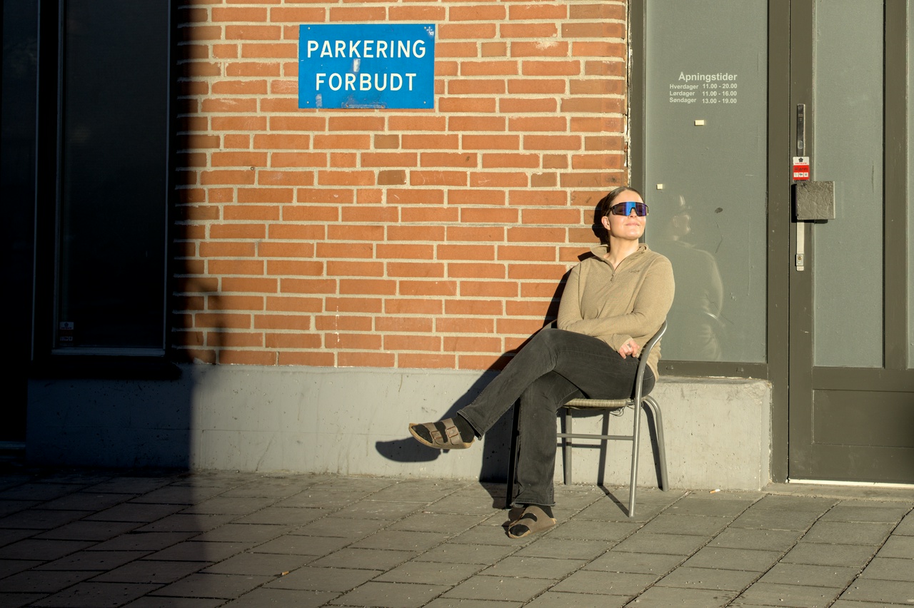 en dame sitter i sola utenfor en murvegg