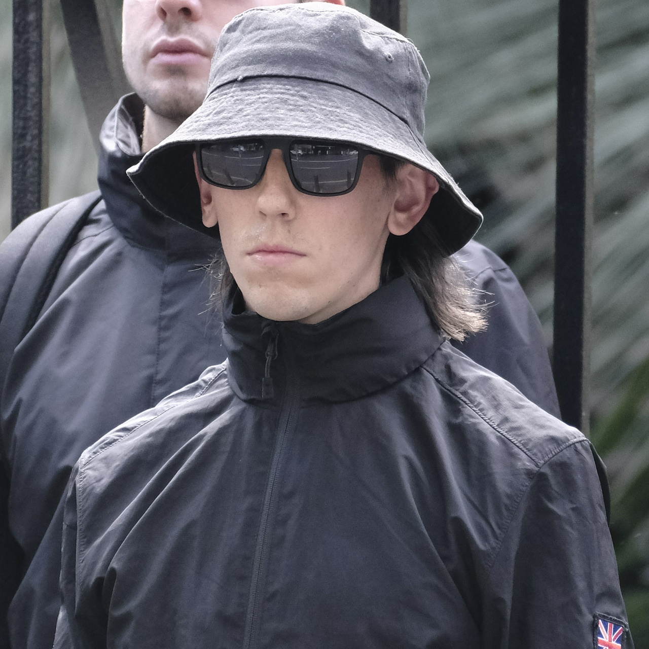 A very short man with a straight black mullet and huge ears under a bucket hat and sunnies