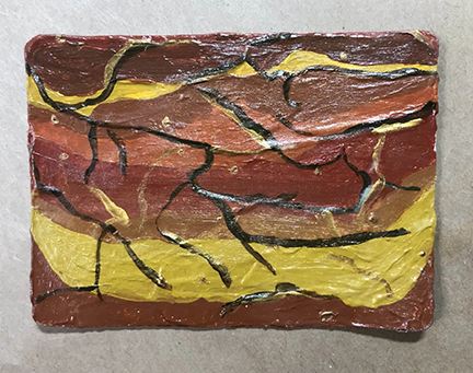 a rectangular magnet with rounded corners, painted with layers of browns and oranges and ochres. Darker brown veins run through, and flecks of gold are visible. The lighting - harsh white from above, creating shine blowout and hard shadows - isn't helping matters. 