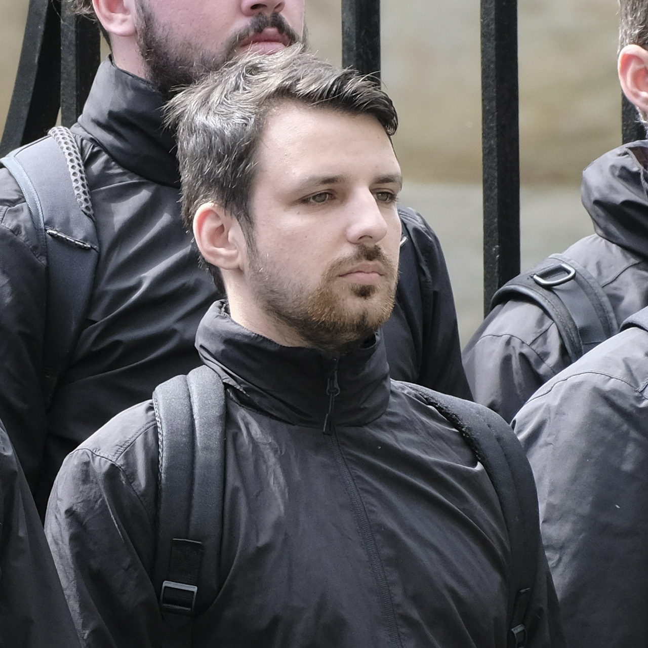 A short thin man with messy dark hair, a beard with tufts of ginger, and vacant hazel eyes