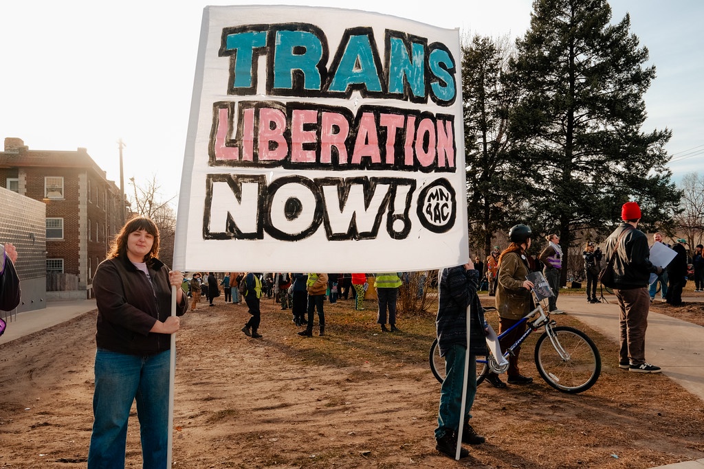 Protestors hold a banner calling for “Trans Liberation Now!” as supporters gather on the Walker Library Lawn. 