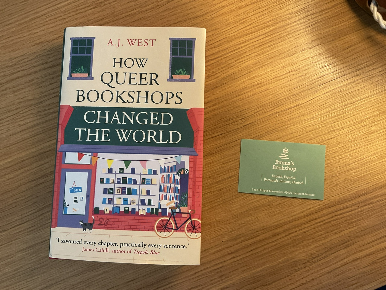 Image of book on a desk. The title is How Queer Bookshops Changed the World. Author's name is A J West.