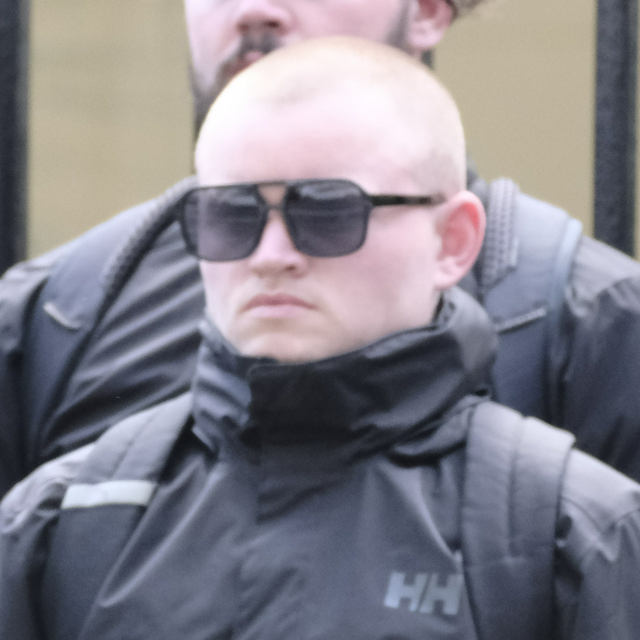 A stumpy bald guy with a very round head and narrow eyes frowns, tucked into his jacket