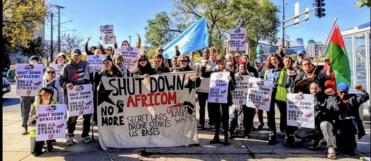 A group of protesters holding signs, flags, and a banner.