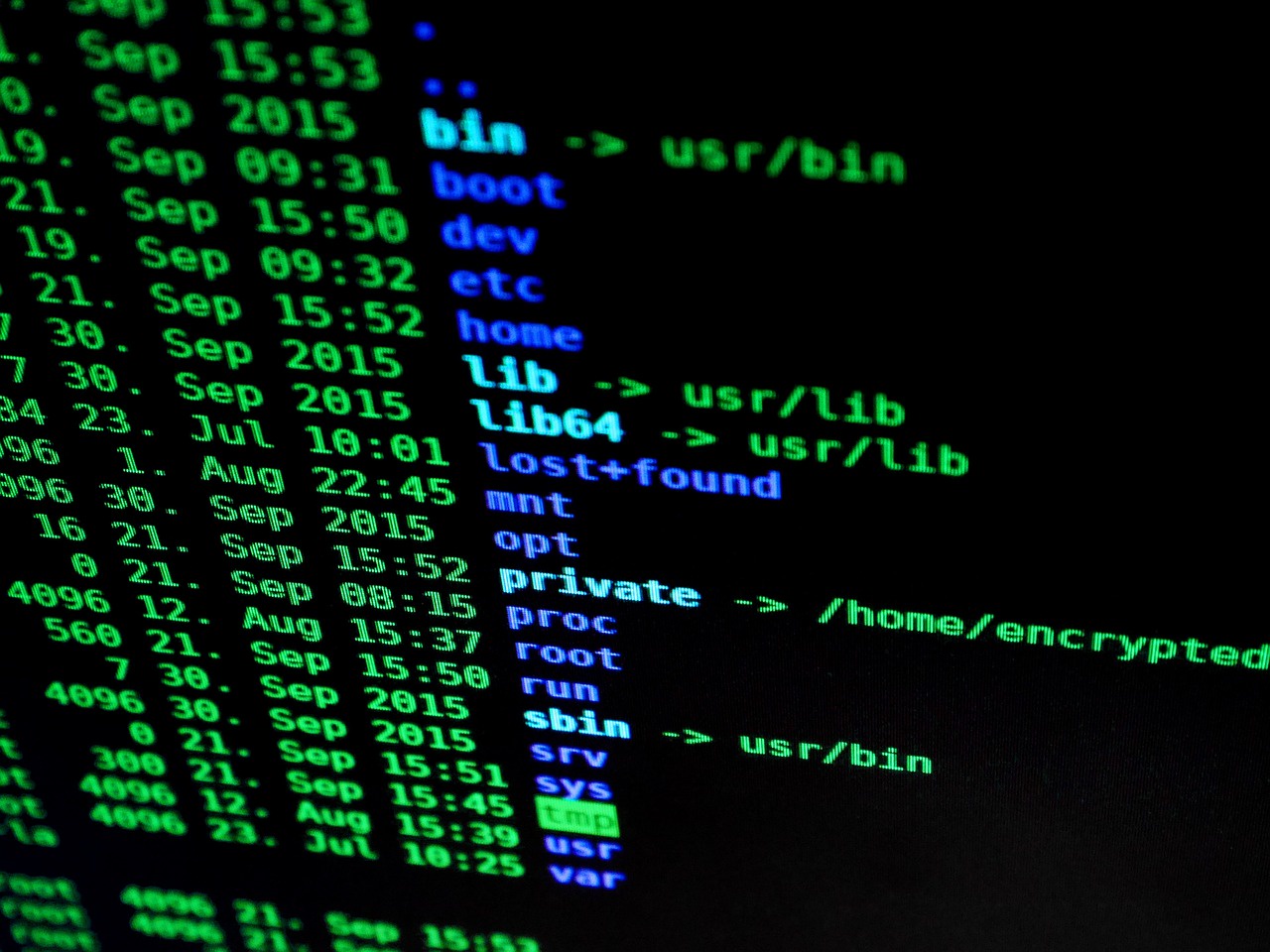 A picture of an LCD computer screen taken at an angle. The screen shows a close up image of the output of an ls command in the root of the drive. The ls output is color coded and shows sym links in light blue.