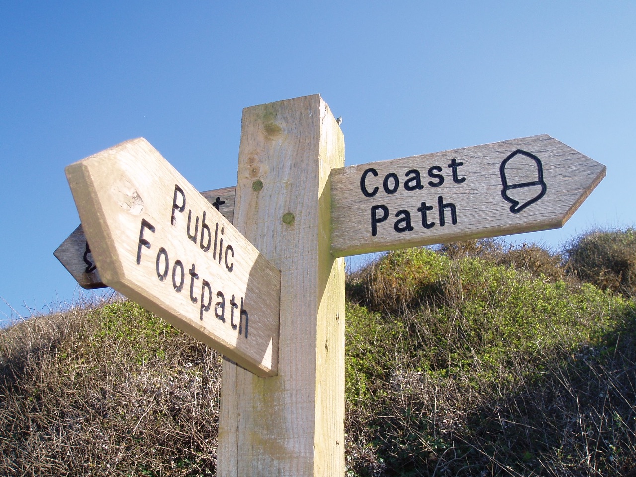 A wooden signpost with writing that says Coast Path and footpath.