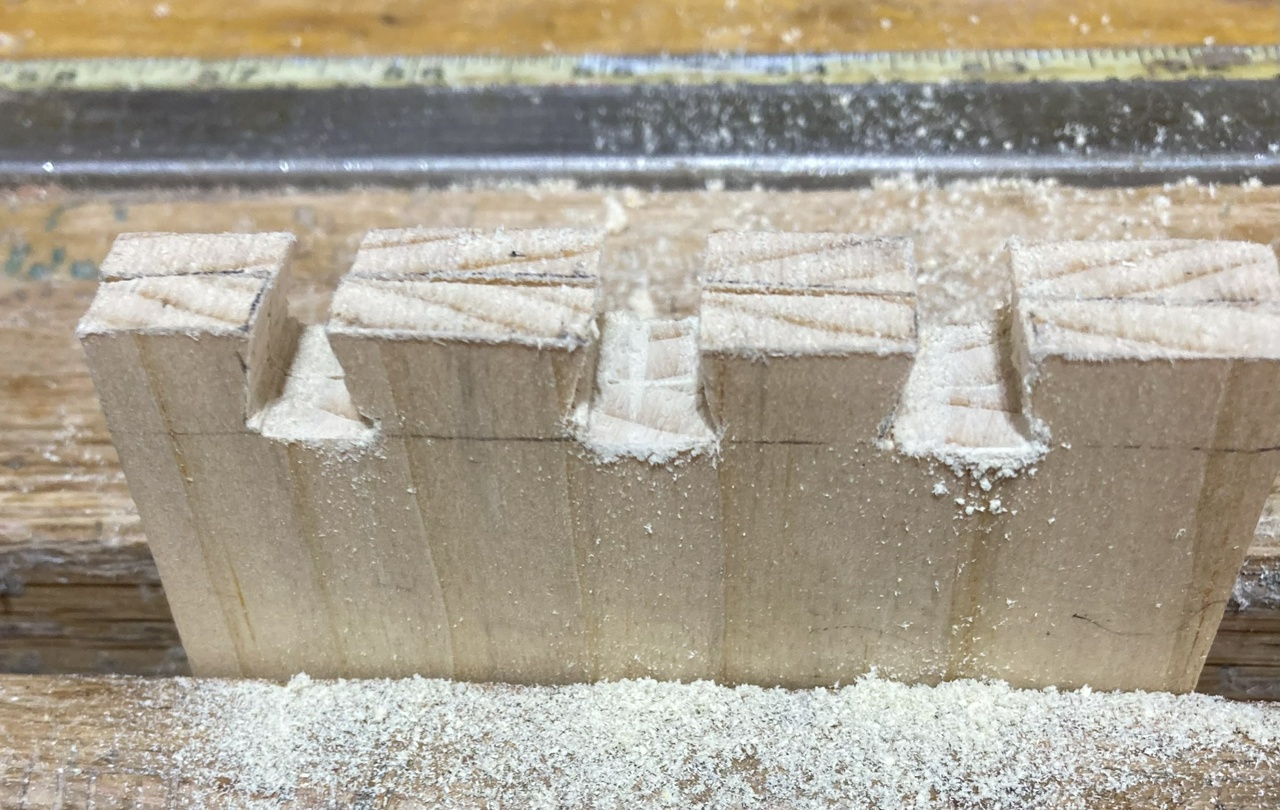 three dovetails cut in two boards held in a face vise, with sawdust near the boards