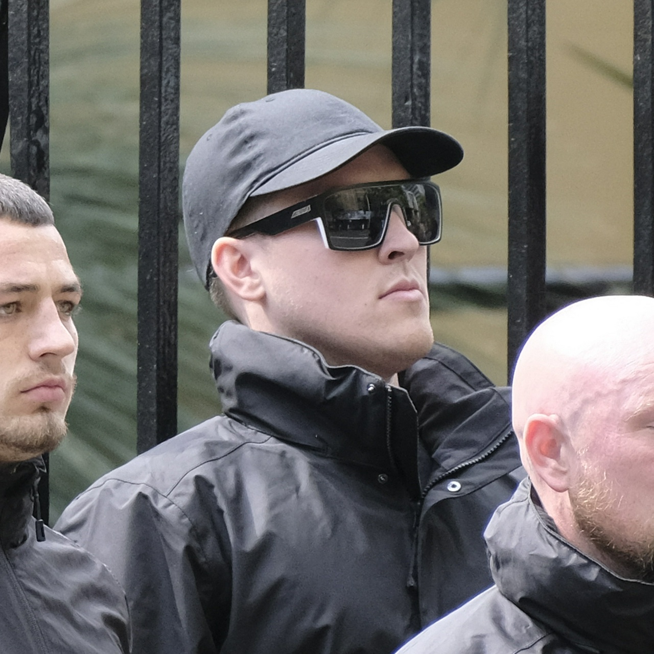 A very chin-heavy white man with small ears, black cap and chunky black sunglasses with white trim