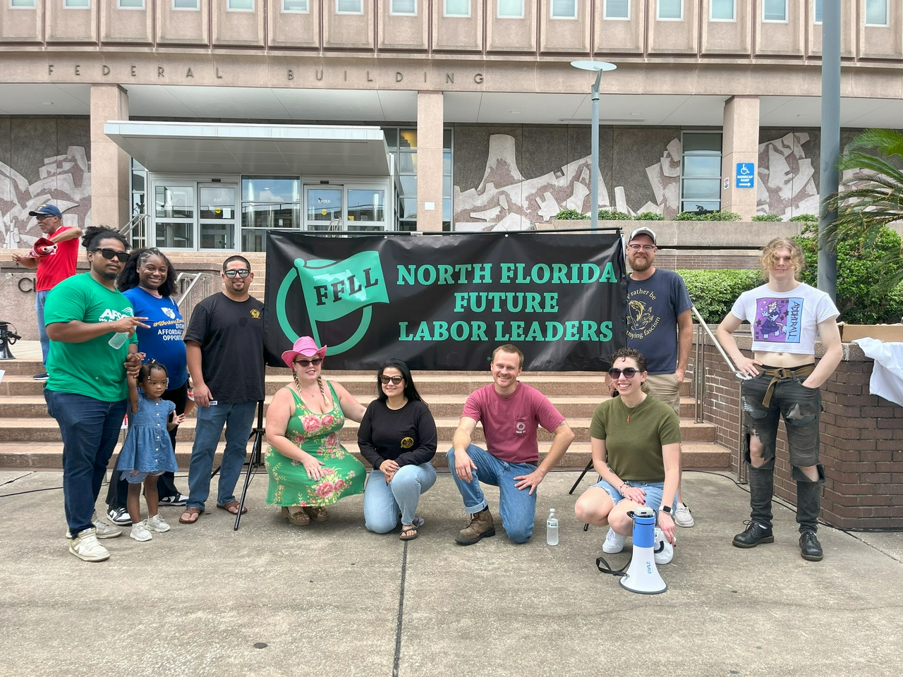 A group of protesters pose in front of a banner that says, 