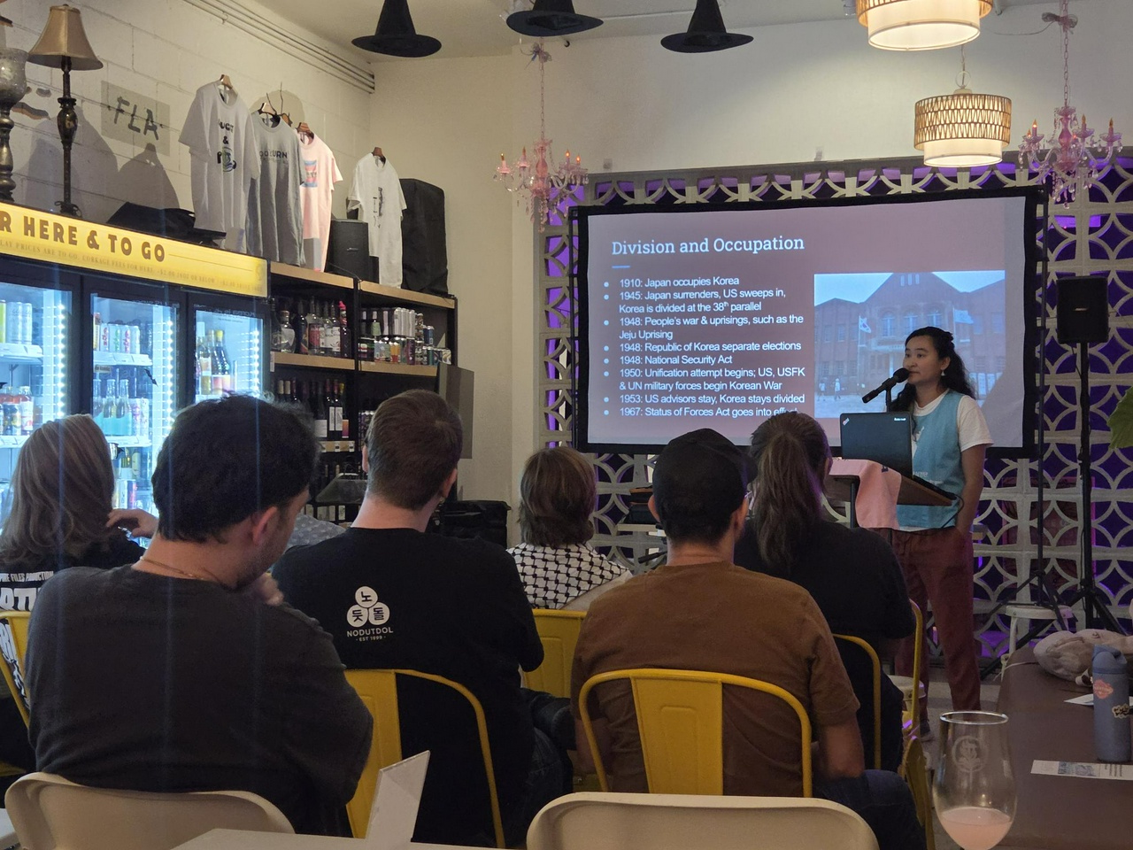 A woman speaking at a microphone to a room of people. 