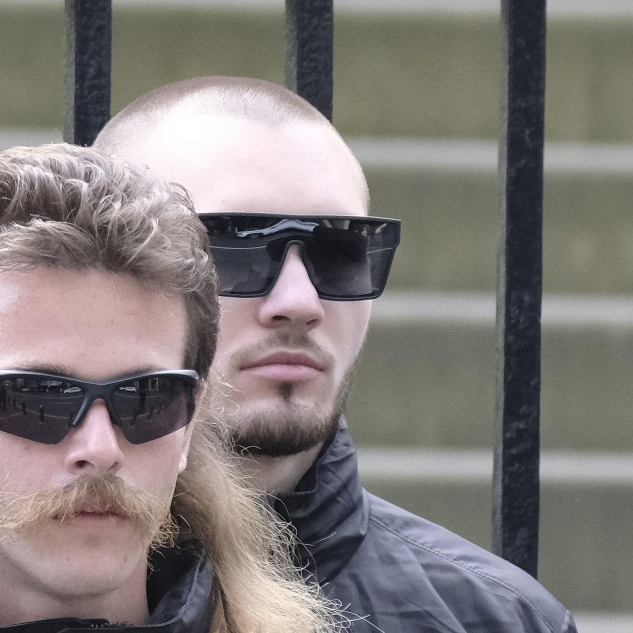 A balding man with a buzzcut and a light beard wears very large flat top sunglasses