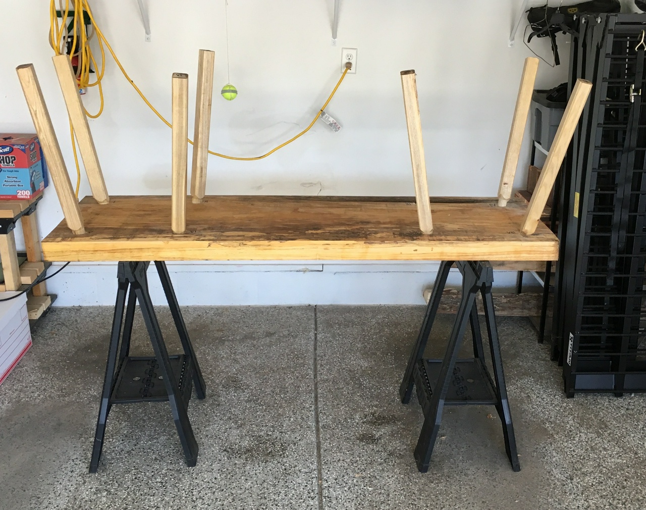 Bench, resting upside-down on a pair of sawhorses, with seven of the eight legs fitted in place