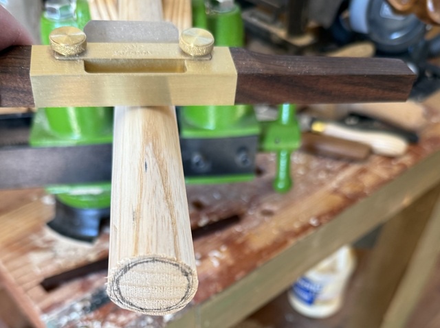 A cane shaft is held in a carving vise, and a large spokeshave sits atop the shaft - the end of the shaft has a circle drawn on it to guide my carving