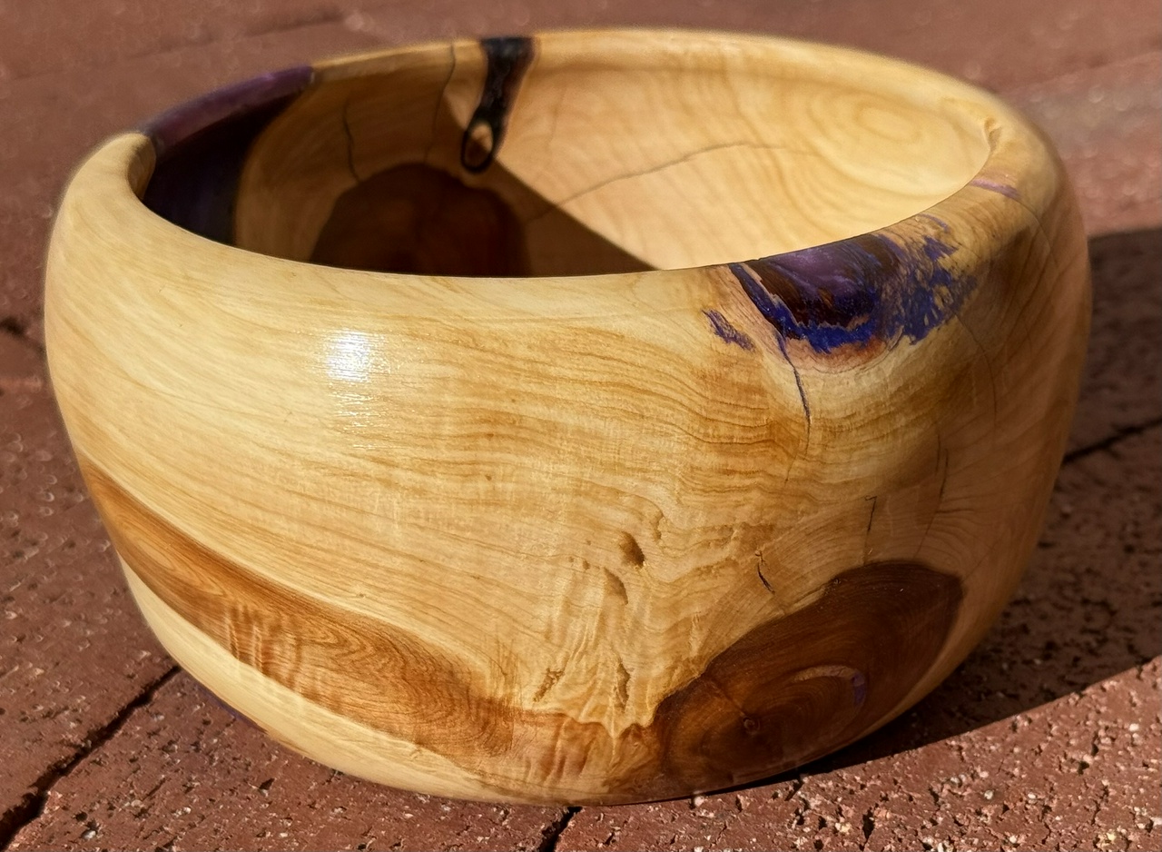 A juniper bowl with purple and blue resin filling flaws in the wood.