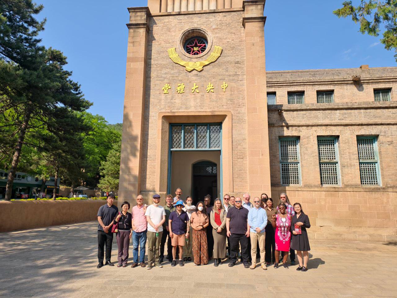 A group of people standing in front of a meeting hall with Chinese characters over the entrance.