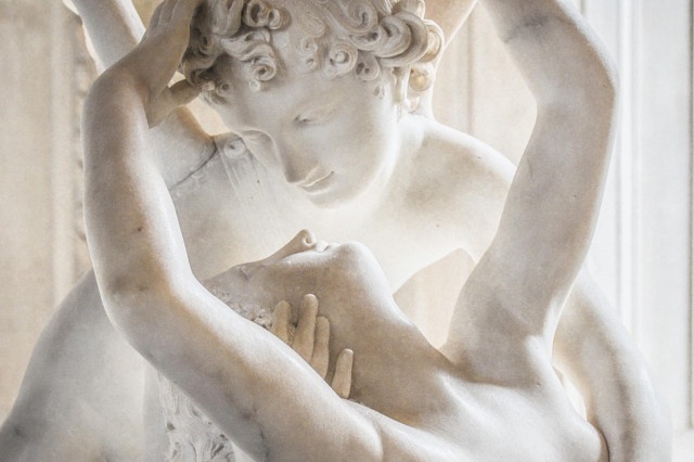 Two statues in an embrace. The top statue appears to have wings. It looks down lovingly at the other statue in its arms and puts a hand on the side of the face and neck of the other statue. The other statue holds its arms above its head with one hand in the hair of the top statue and the other hand stretching up out of frame. Bowdlerized cropping done by yours truly to avoid social media site nonsense.