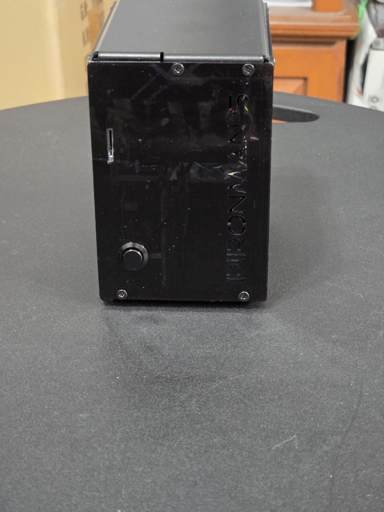 A black, vertical standing computer case with a glossy finish and the word "PIRONMAN" embossed on the front, placed on a textured gray surface. The case features visible ports and a power button on the front panel.