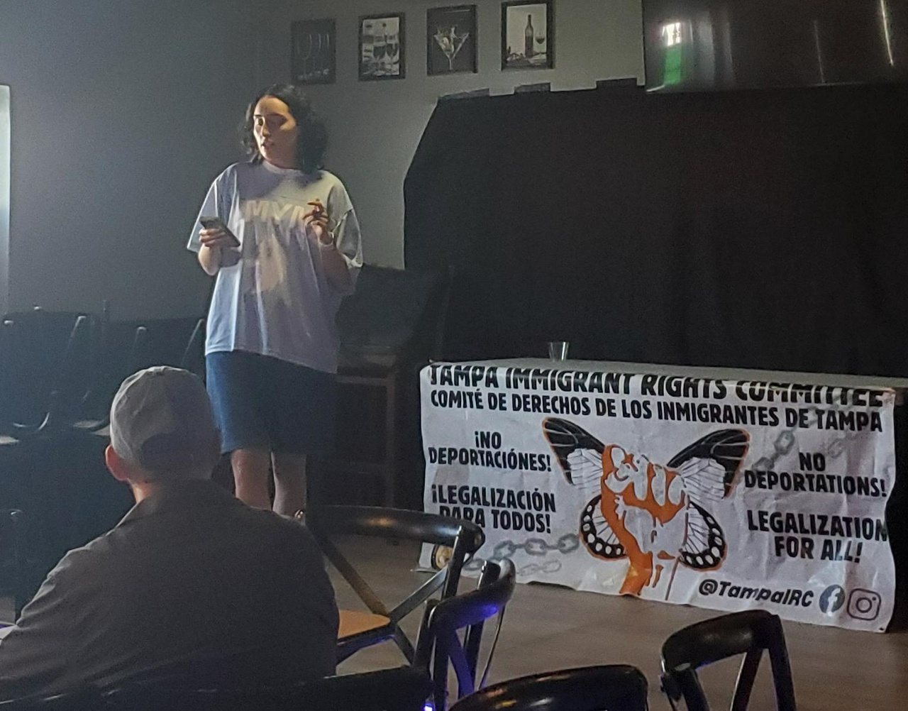 A speaker stands in front of a room and reads a speech in front of a banner that says, 