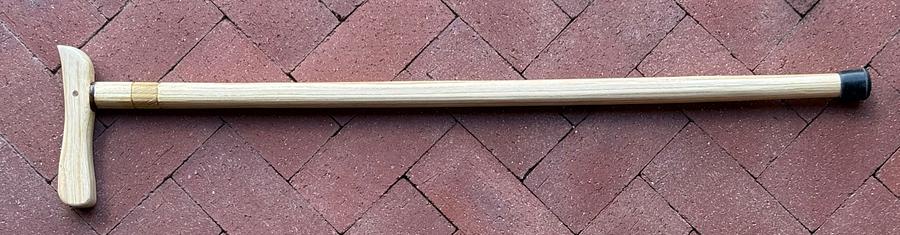 The cane, laying flat on a brick patio, the handle pointing down from the left end of the shaft