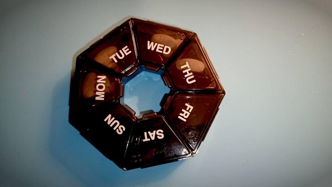Photo of a circular pill sorter box against a pale blue background. Photo by Unattributed.