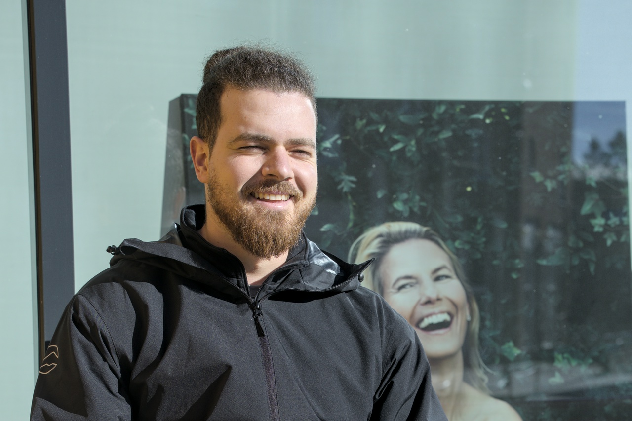 Leart En mann smiler/myser med sola i ansiktet. Bak ham skimtes en reklameplakat med en dame som ler overdådig