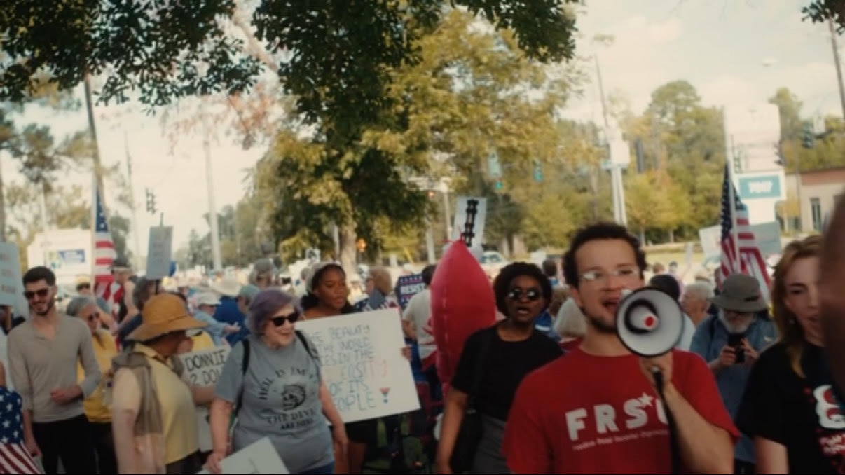 Large crowd  at the No Kings  event chanting as they march down the sidewalk.