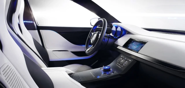 The front cabin of a futuristic concept car. It's mostly white with electric blue lights near the dashboard, console, and manual controls.