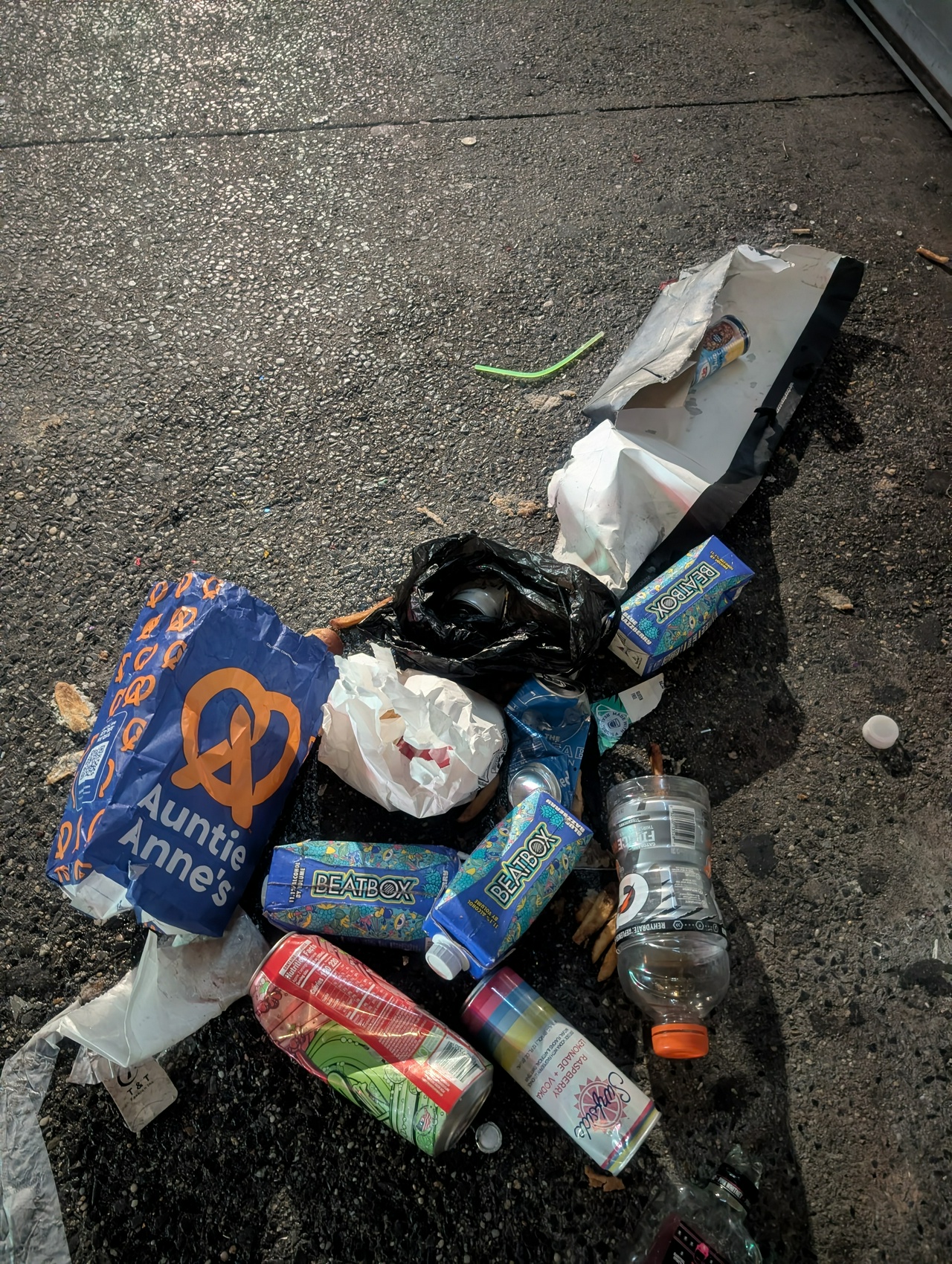 a melange of sidewalk trash that includes an Auntie Anne's bag and empty containers of Beatbox, Gatorade, Surfside, and more