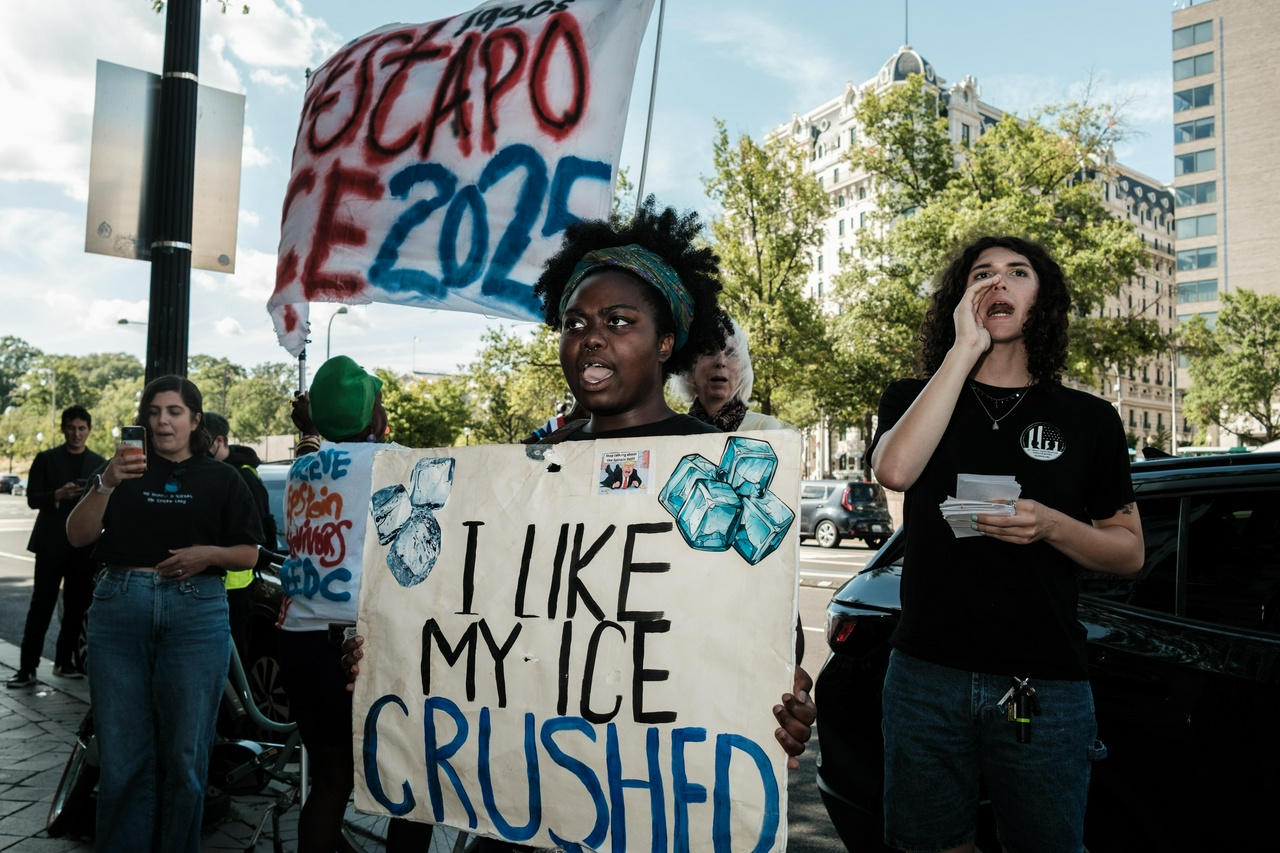 A group of protesters protest in front of the mayor's office and city council building and hold signs that say, 