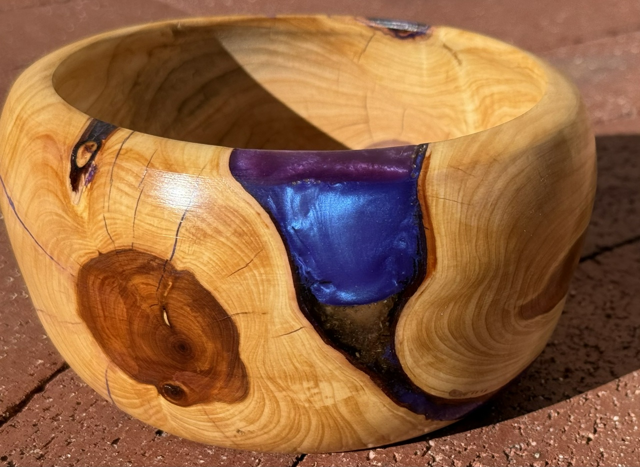 A juniper bowl with purple and blue resin filling a bark inclusion within the wood.
