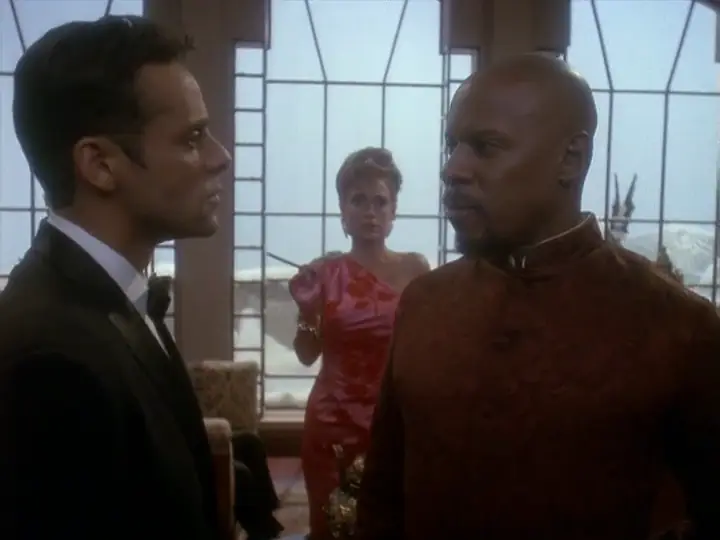 Avery Brooks, Alexander Siddig, and Nana Visitor play characters in a spy thriller holonovel. Avery looks at Alexander skeptically while Nana watches from behind holding a cigarette holder in her hand.