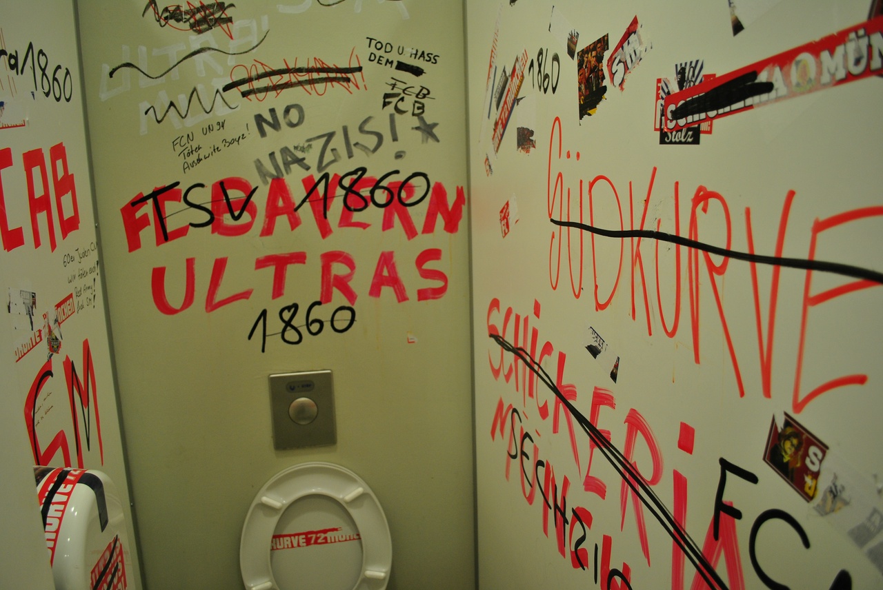 A public bathroom with boisterous comments written on the walls. Most text is not in English, but the phrase "No Nazis!" does appear.