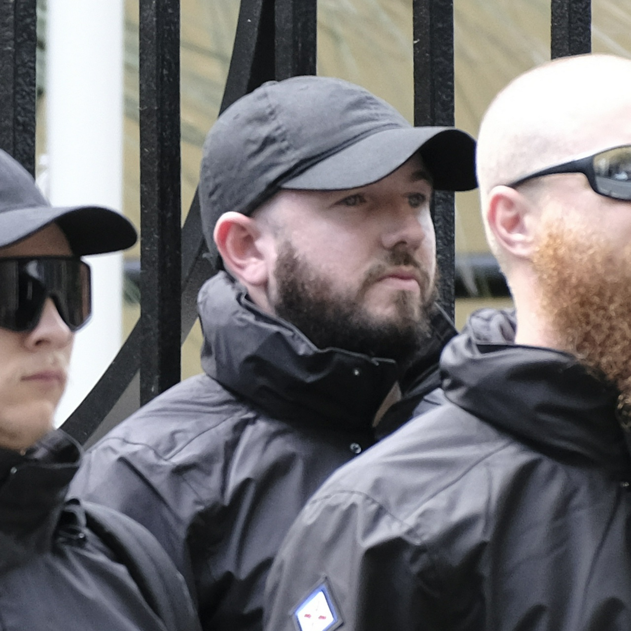 A tall balding man with a dark beard and black cap